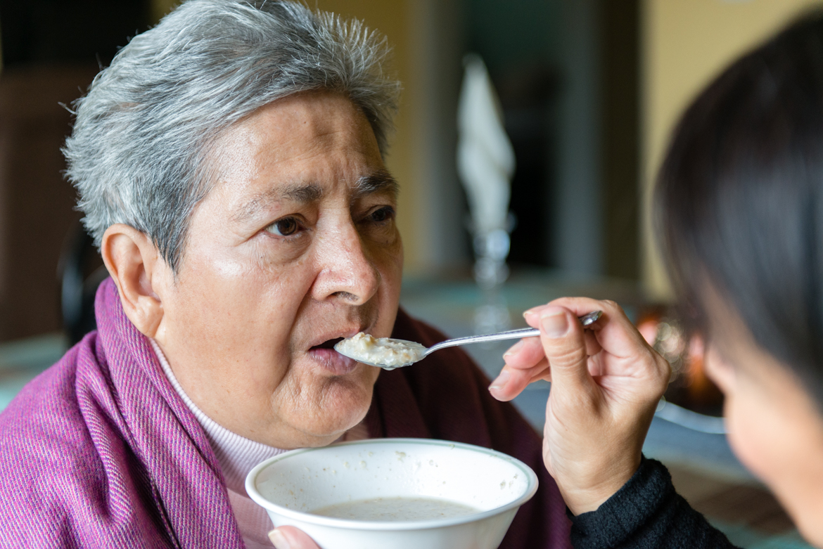 Tania Yanes feeds oatmeal to her mother, Blanca Rosa Rivera. “My mom is 100 percent dependent on us.” says Yanes. (Heidi de Marco/California Healthline)