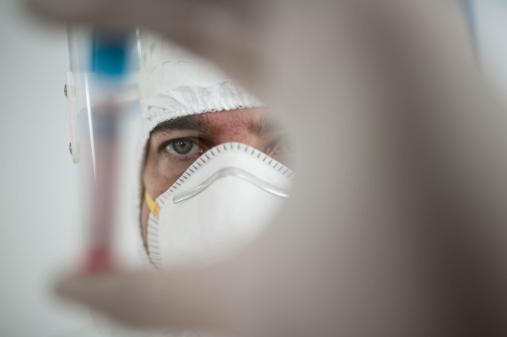 In a chemistry lab, a male researcher holds a tube with the coronavirus virus