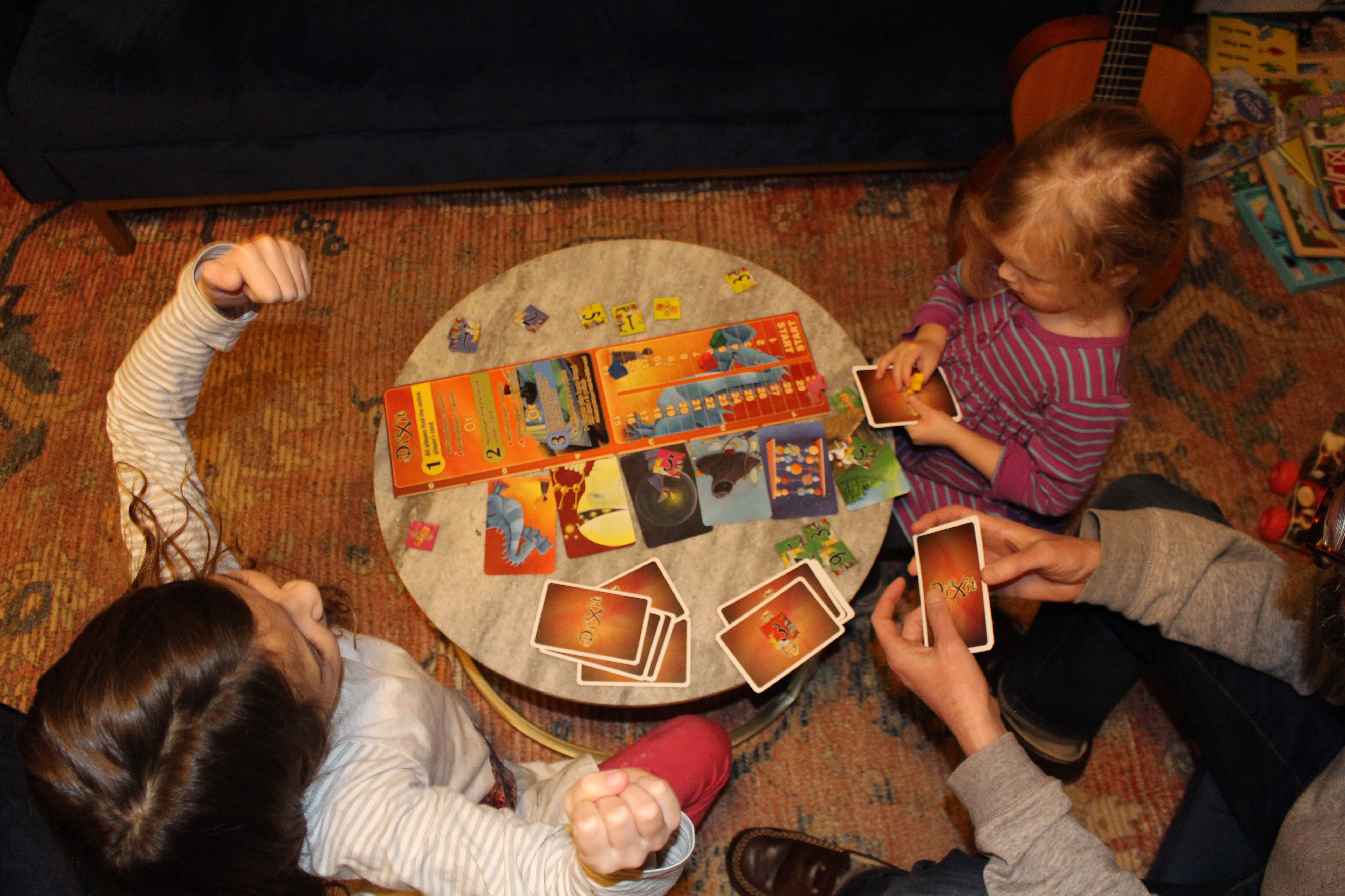 बच्चे टेबल के चारों ओर बैठकर ताश का खेल खेलते हैं।