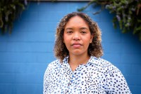 Daisha Williams stands in front of a blue wall in North Carolina. Greenery peaks over the top of the wall.