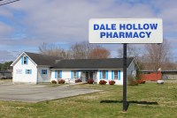 A large sign that reads, "Dale Hollow Pharmacy," in blue lettering stands in front of Dale Hollow Pharmacy. The pharmacy is a white building with a grassy area and parking lot at the front.