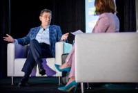 Albert Bourla is seen sitting in a chair, speaking during a panel at the South by Southwest festival. A blurred person sits on the left in the foreground.