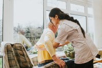 Young care assistant helps an elderly gent put on his jumper