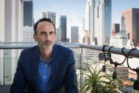 A man sits on a balcony with skyscrapers behind him.