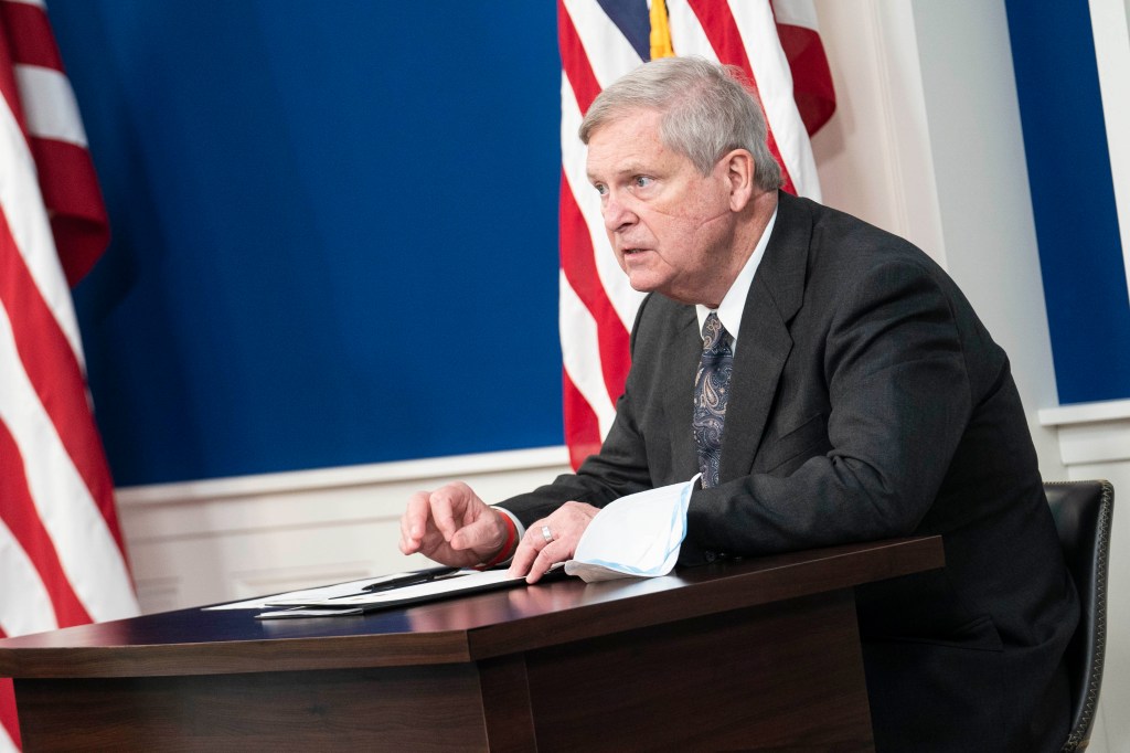 Tom Vilsack is seen sitting at a table, facing to the left. A mask sits on the table in front of him.