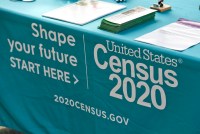 A photo shows a closeup of a table cloth advertising the 2020 U.S. Census. The tablecloth is blue-green and text on it reads, "Shape your future. Start here," and "United States Census 2020."