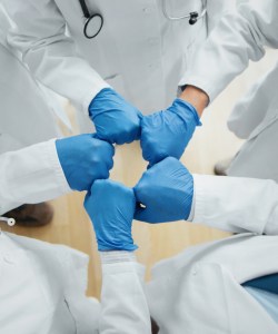 Five doctors in doctors in lab coats and blue gloves fist-bump.