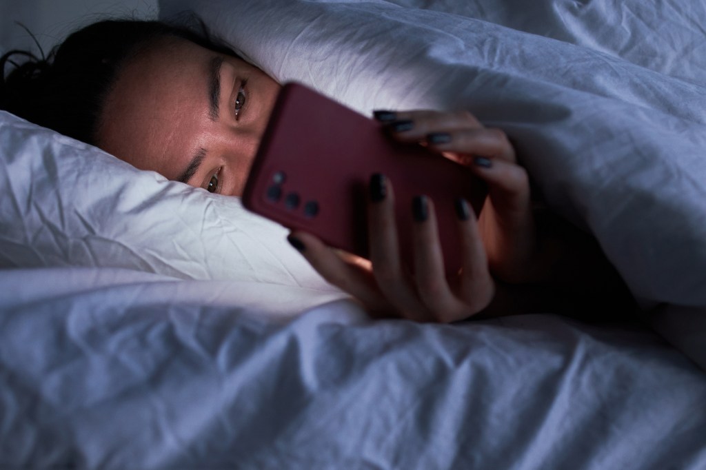 A woman looks at her phone while lying in bed.
