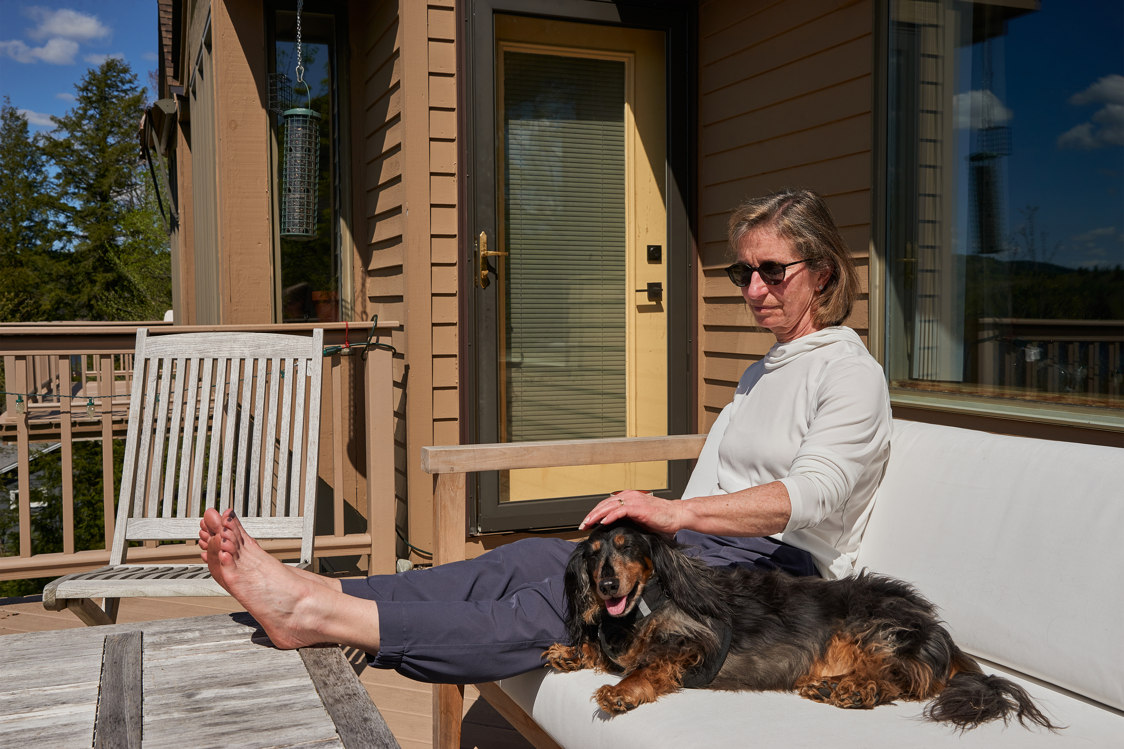 Elizabeth Melville sits outdoors wearing sunglasses. She is petting a dog lying next to her.