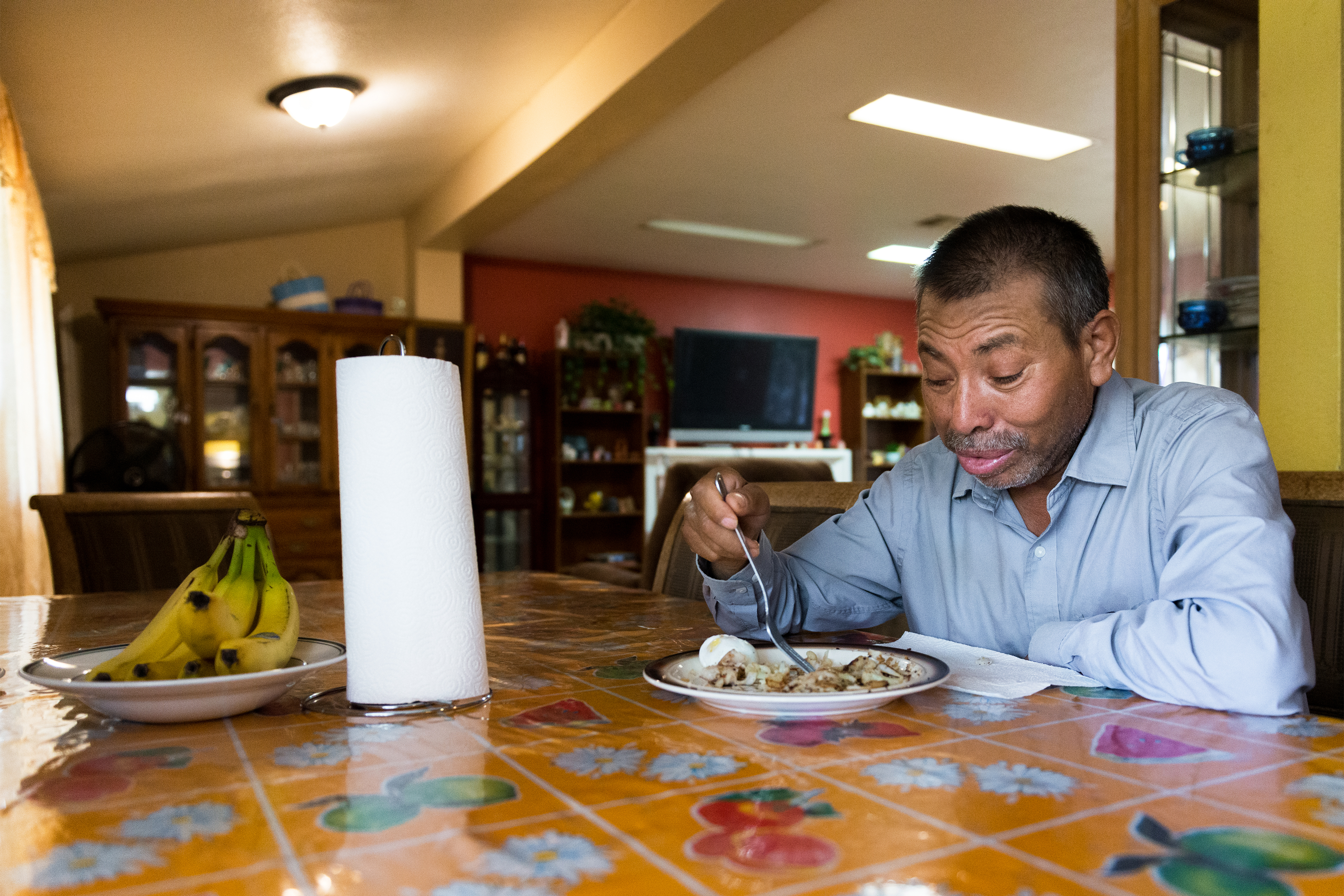 Vidal Fonseca is seen eating at a table at home. A roll of paper towels and a plate of bananas are also on the table.