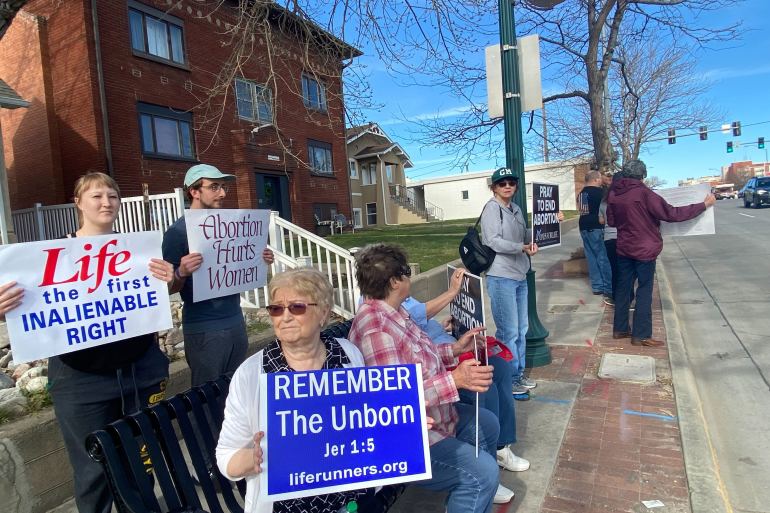 A group of anti-abortion protesters outside of the clinic. They hold signs that read, "Abortion Hurts Women," "Remember the Unborn," "Pray to End Abortion," among others.