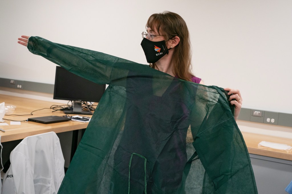 A photo shows Karen Haberland holding a green disposable isolation gown in front of her.