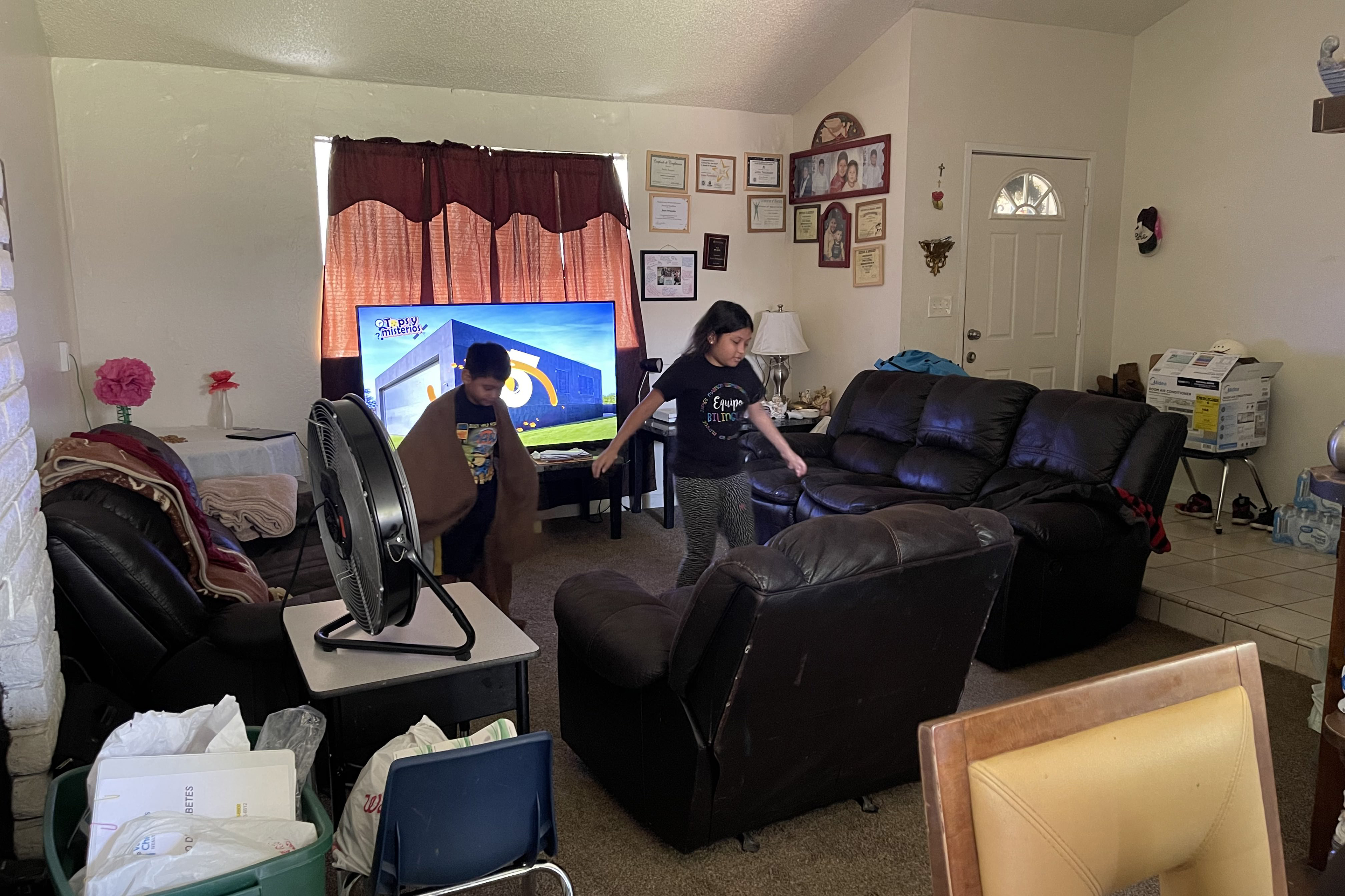 Two children run around a living room. 