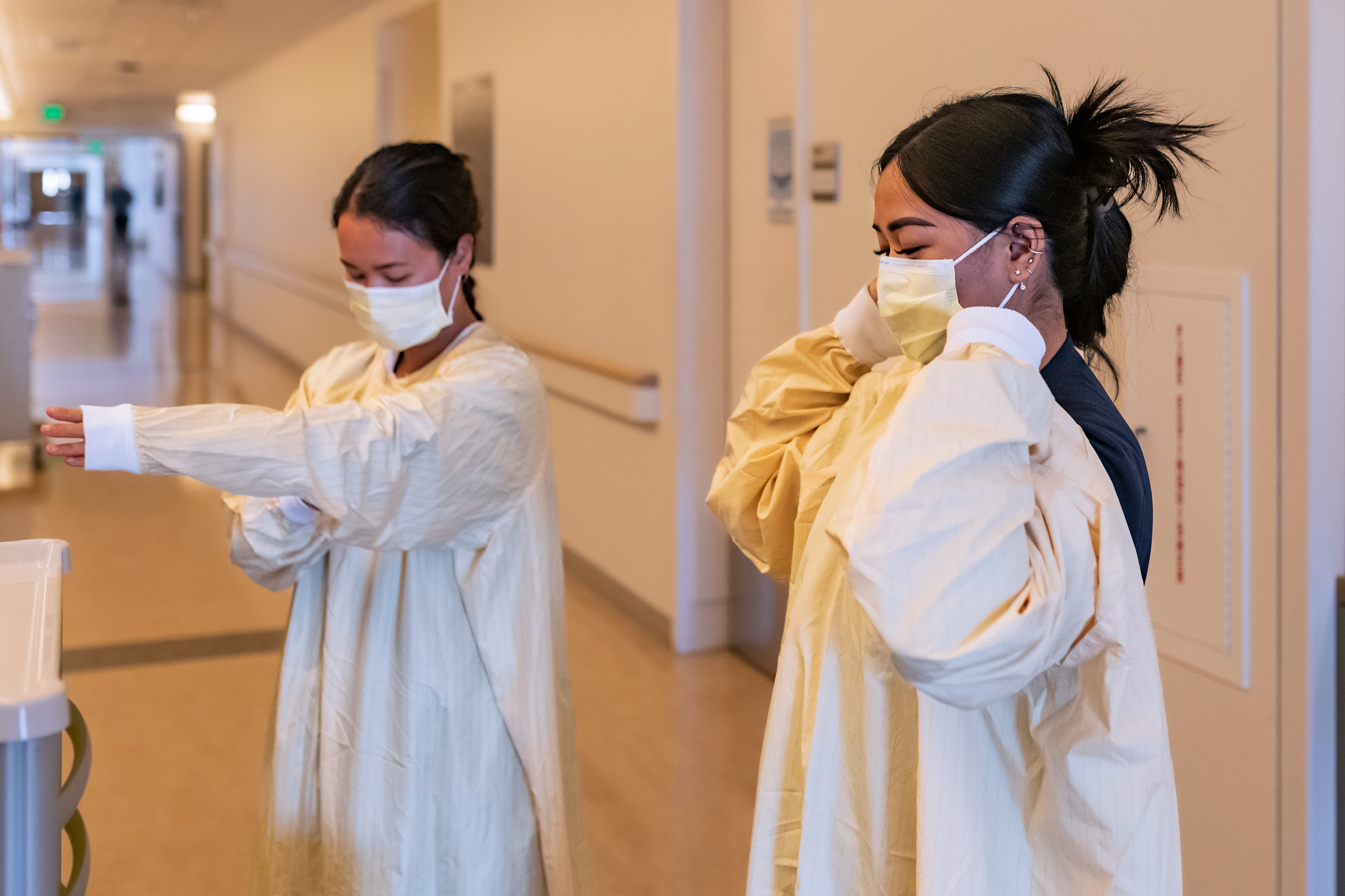 A photo shows two nurses putting on reusable isolation gowns inside of a medical center.