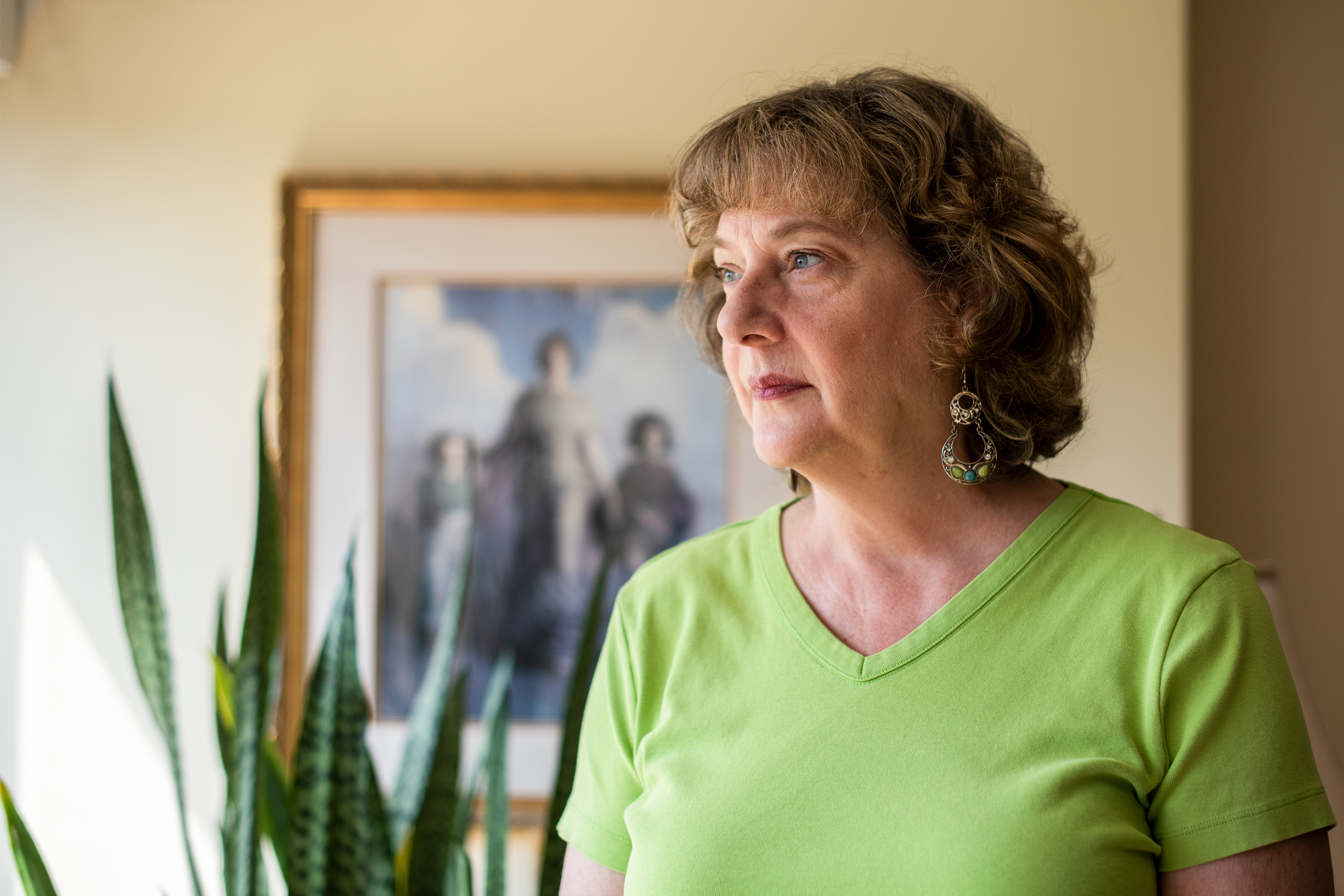 A photo shows Cynthia Martens at her home. She is standing by a window and looking outside.