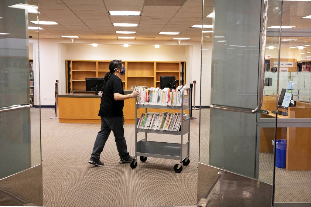 A photo shows a library worker pushing a cart filled with books.