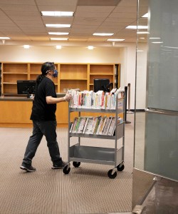 A photo shows a library worker pushing a cart filled with books.