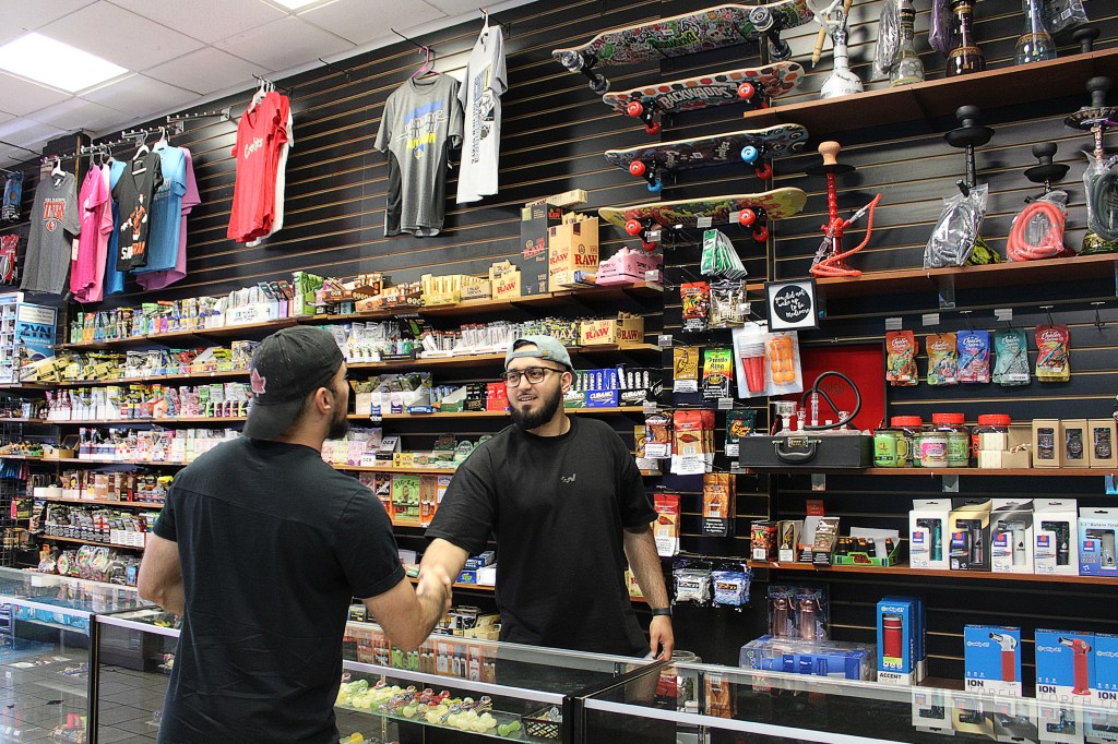 A photo shows John Tokhi helping a customer inside of the smoke shop he co-owns.