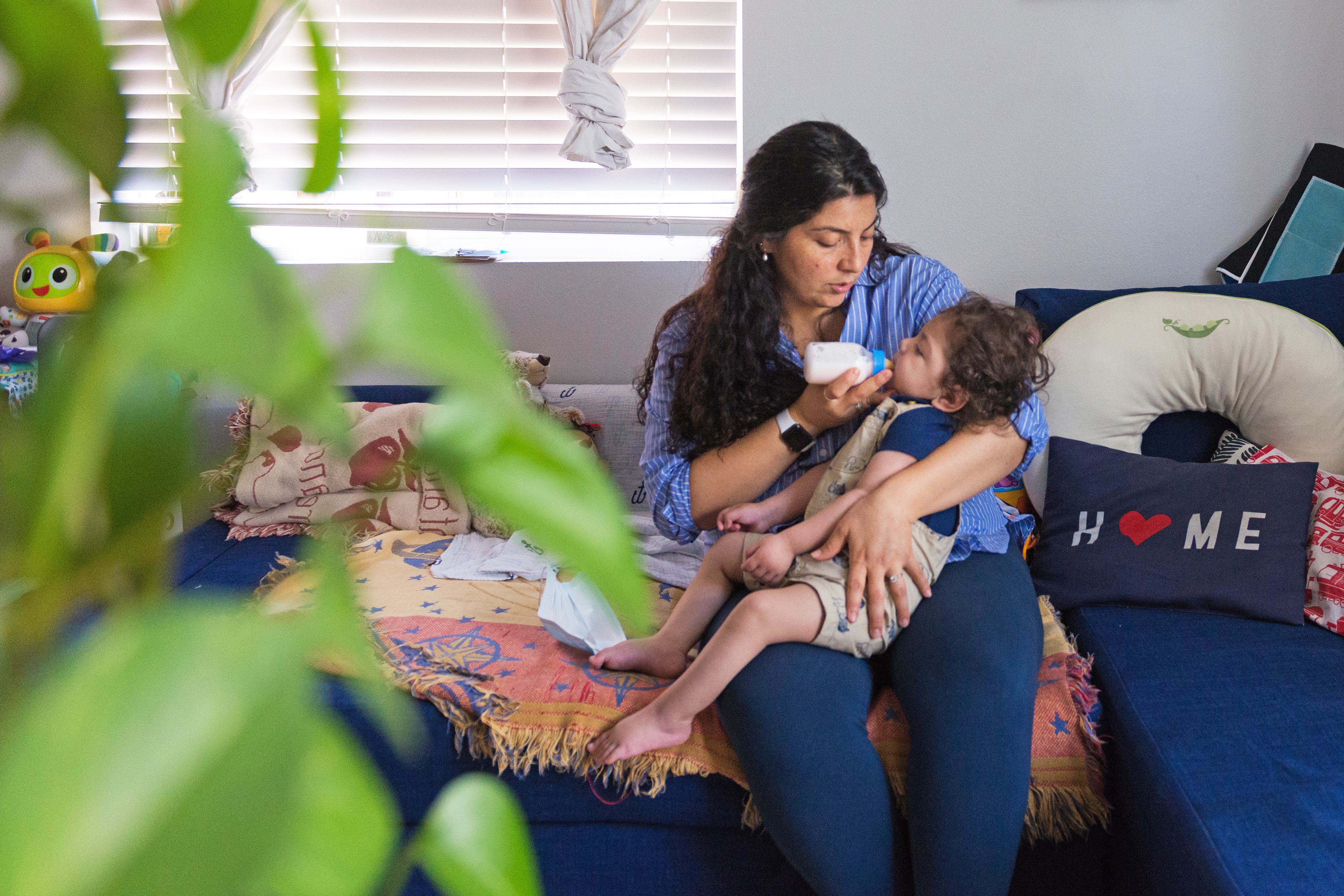 A photo shows Adriana Pinedo sitting at home and feeding her son, Aaron, with a bottle.