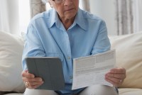 A photo shows an elderly woman looking at bills on paper and at a tablet.
