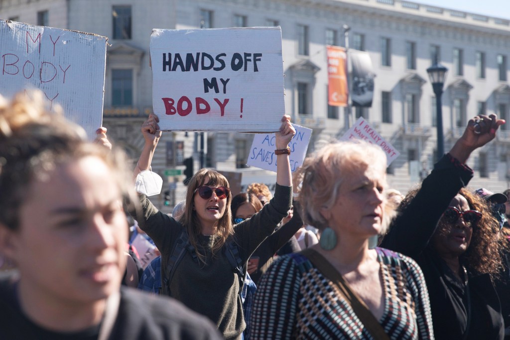 A photo shows a crowd of female protesters. One holds a sign that reads, "Hands off my body."