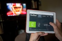 A photo shows someone using a tablet to place bets on FanDuel, an online sports betting service. A football game is seen on the TV in the background.