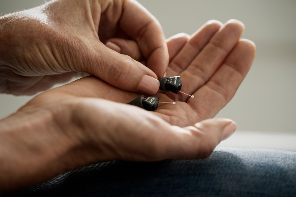 A photo shows a pair of hands holding Sony's new CRE-C10 hearing aids.
