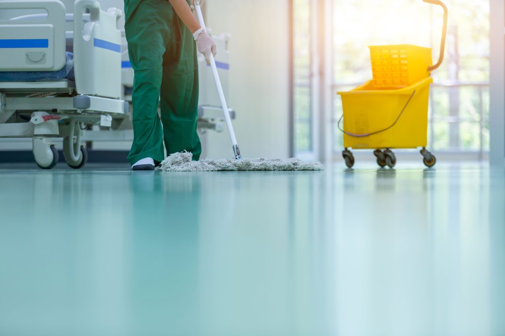 A person with a mop and bucket cleans the floor of a hospital.