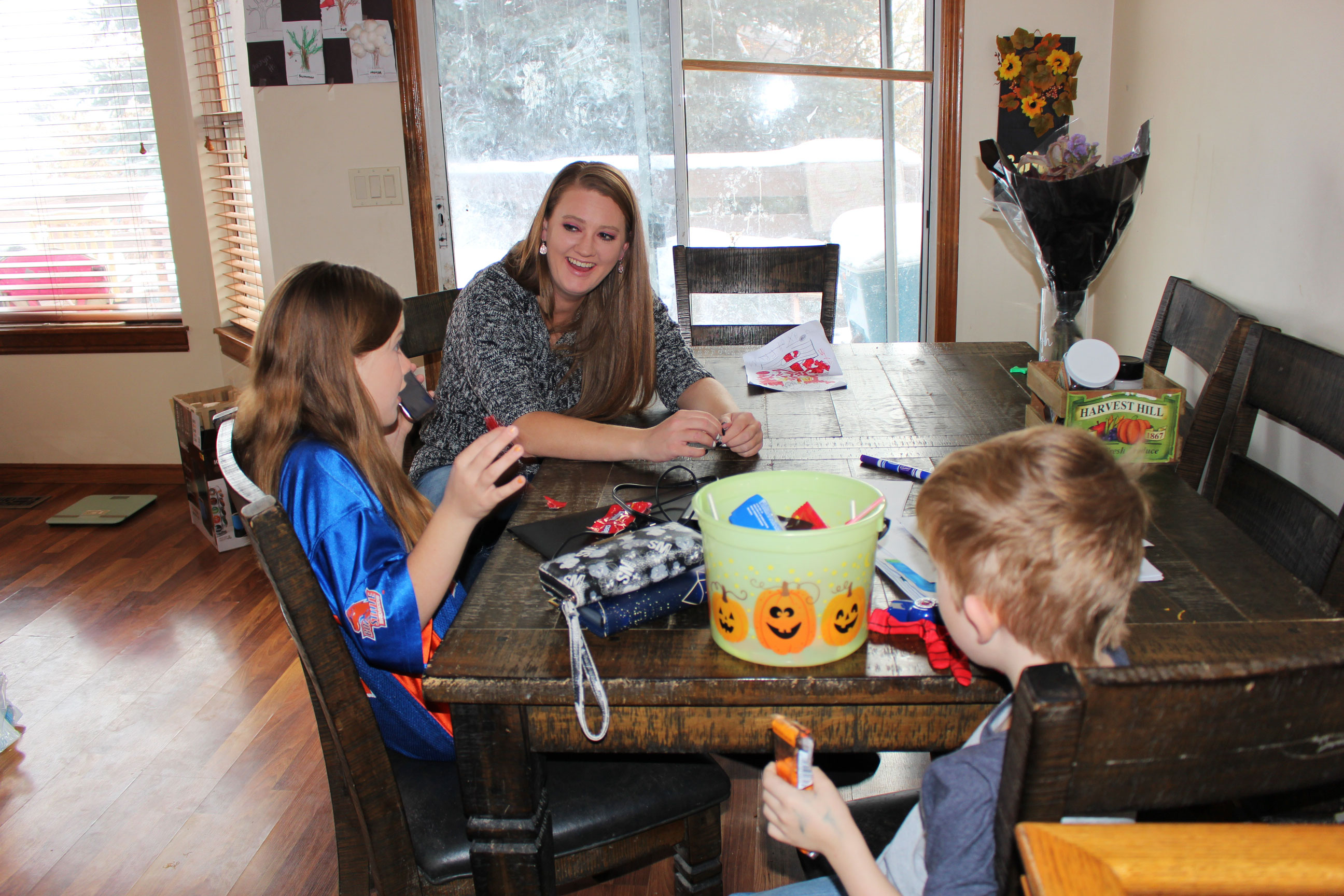 A photo shows Kayla Hopkins at home with her kids. They are sitting at a table.