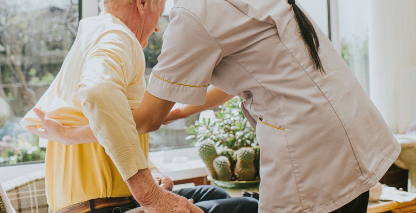 A photo shows a woman caregiver helping an elderly man get dressed.