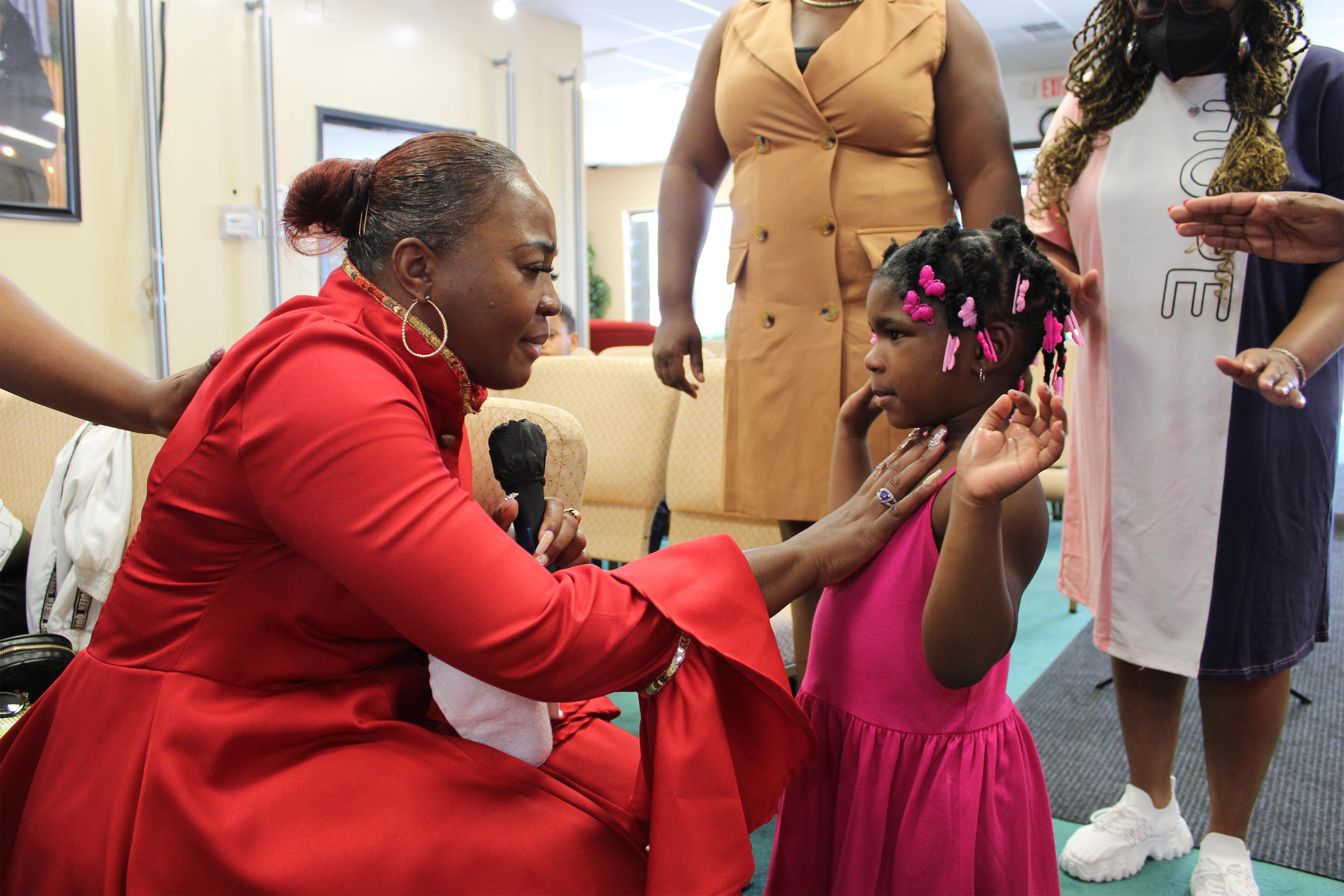 A photo shows April Roby-Bell inside her church, placing a hand on a young girl's heart.