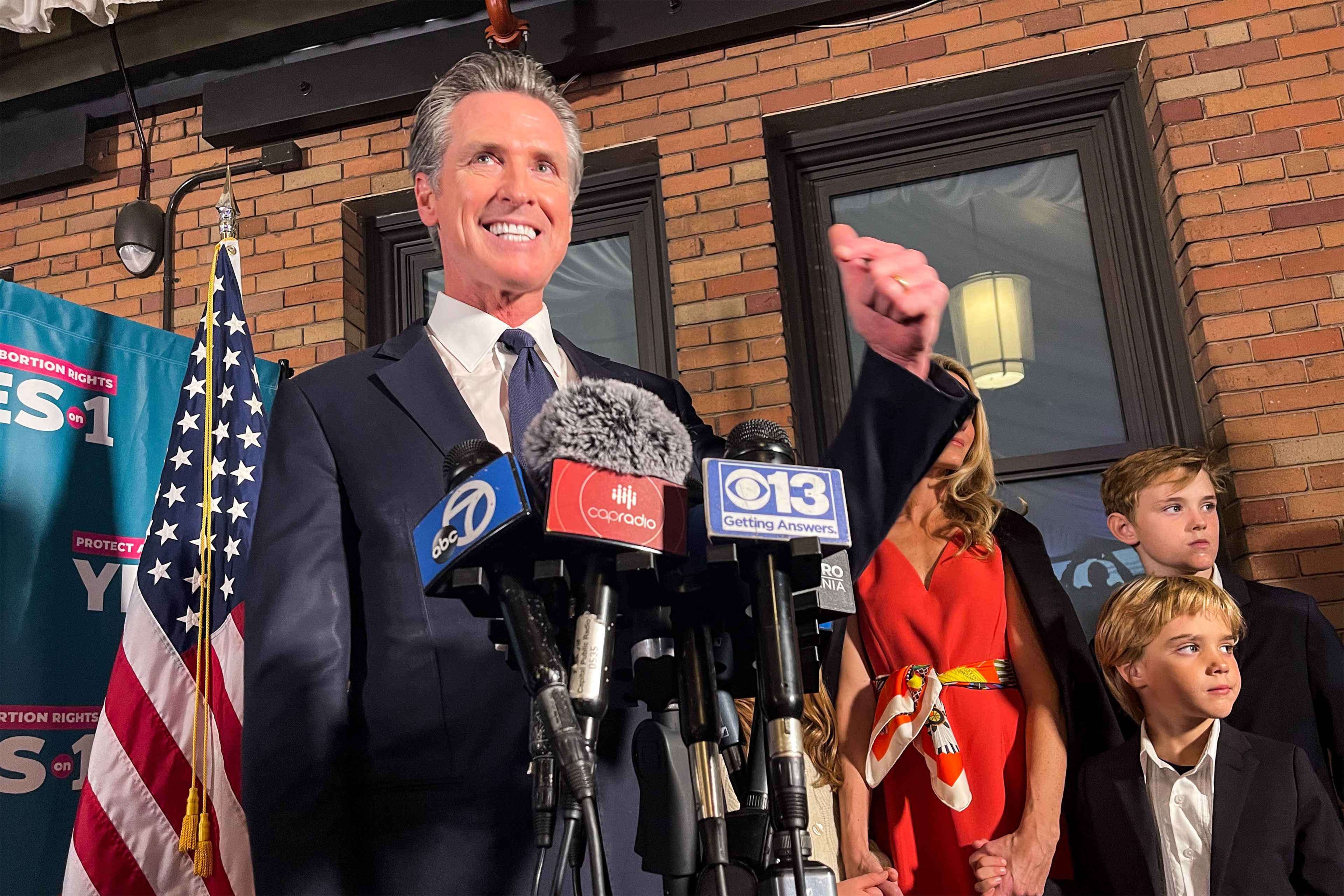 A photo shows Gov. Gavin Newsom at an event with news microphones in front of him.