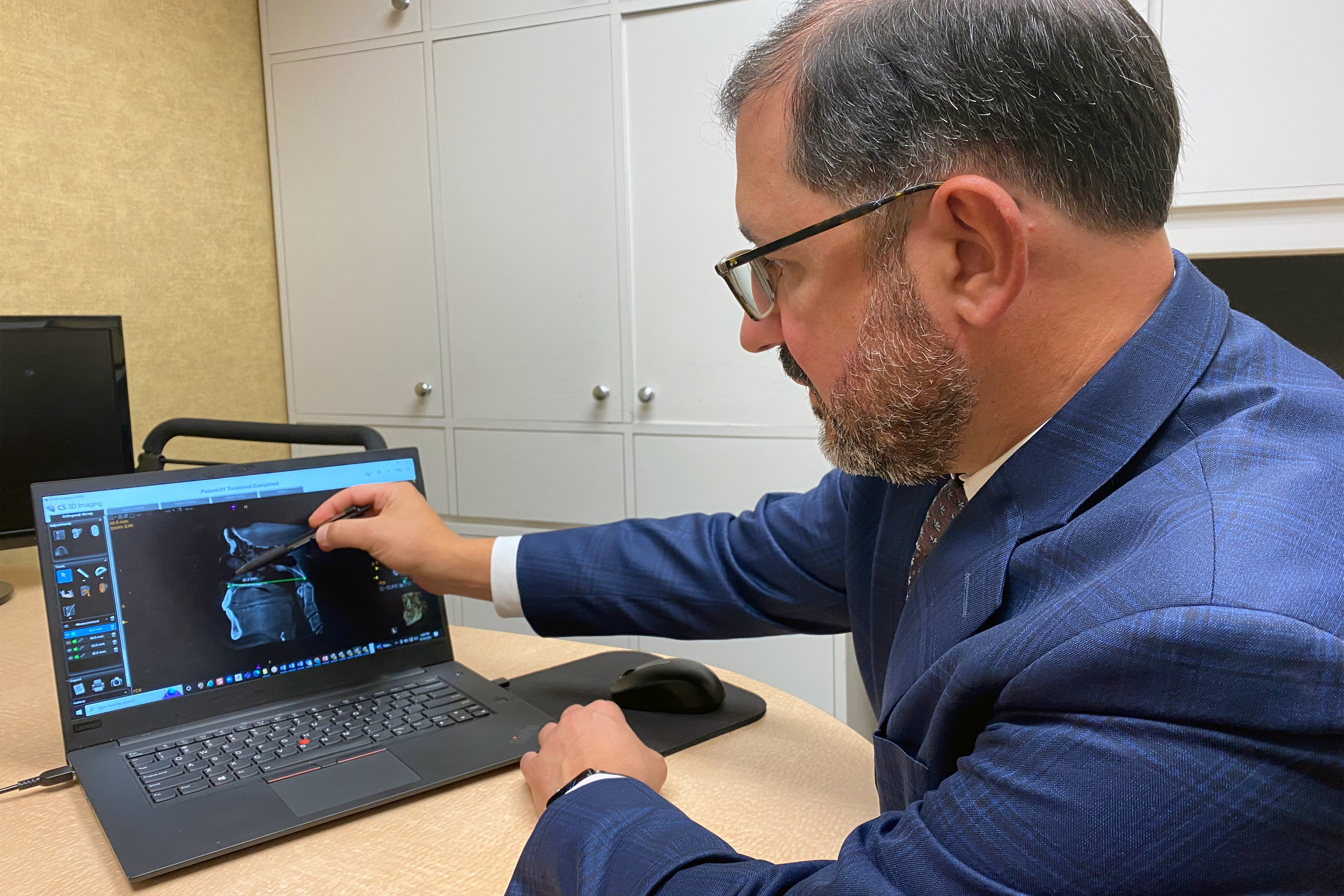 A photo shows a male dental professional pointing to an image of a dental scan on a laptop screen.