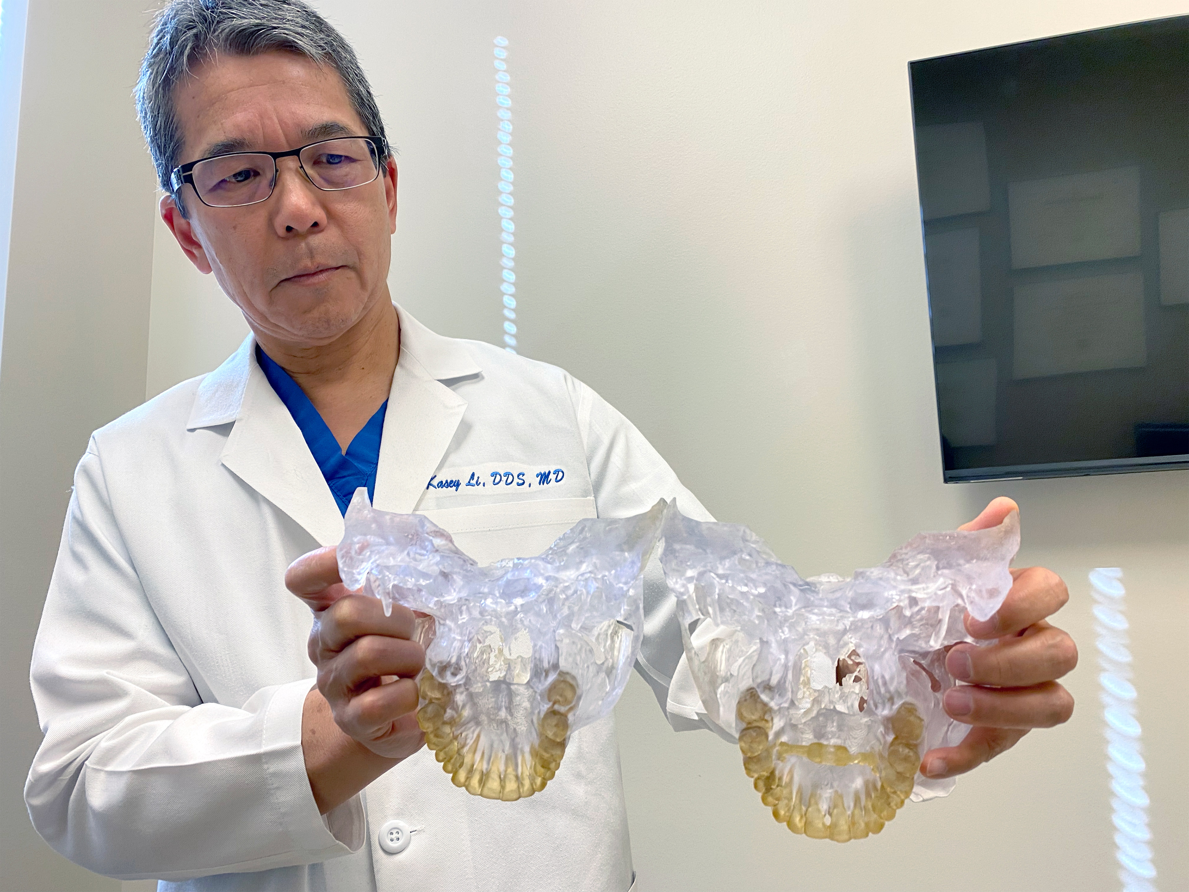 A photo shows a male dental professional holding sculpture models of teeth.