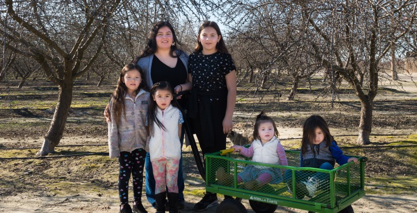 Carolina Morga Tapia stands outside in a park with her five children. Two of the youngest are sitting in a green wagon.