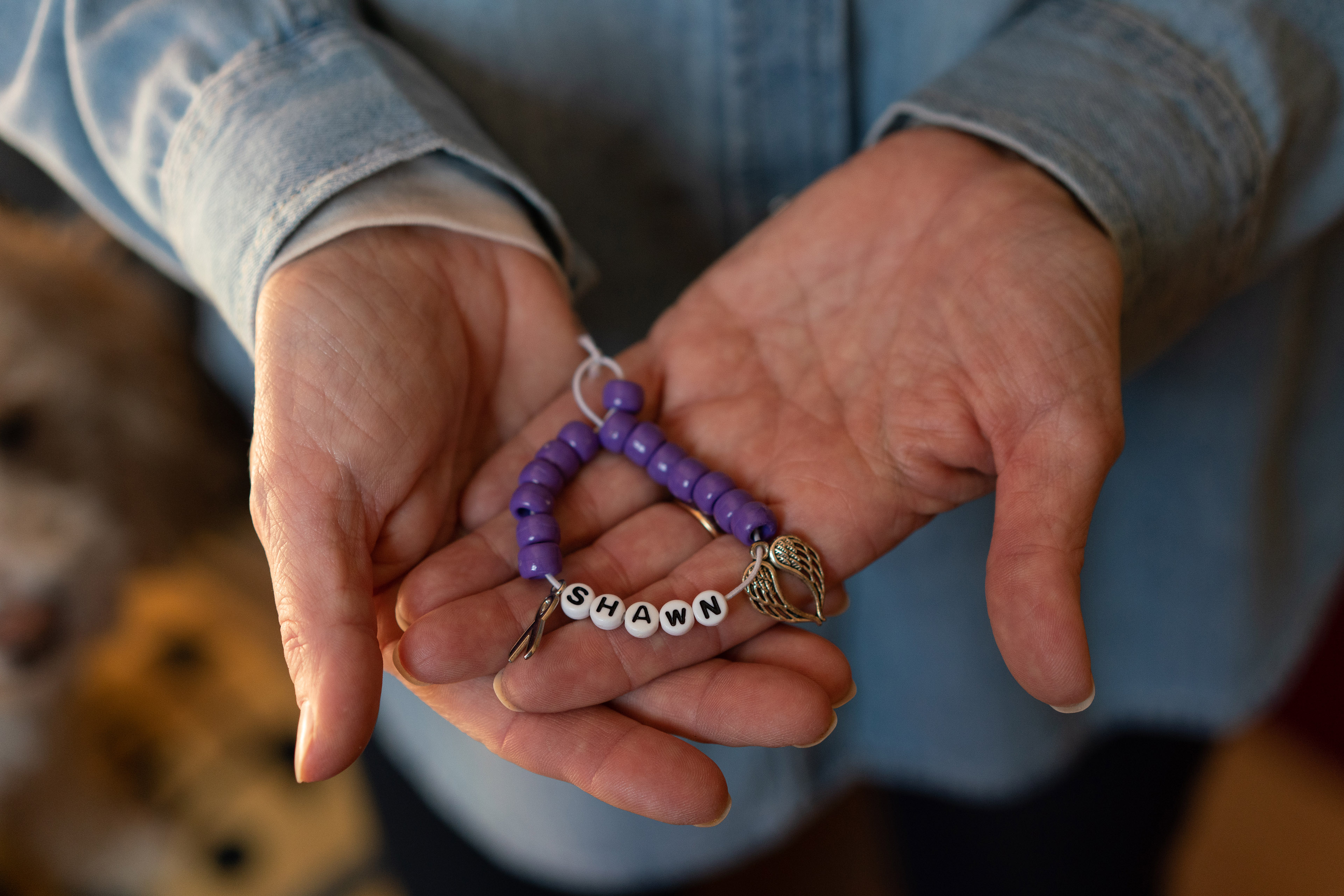 Marianne Sinisi, of Altoona, Pennsylvania, holds in her two hands a purple beaded bracelet with the word "Shawn," in memory of her 26-year-old son, Shawn, whom she lost to an opioid overdose in 2018.