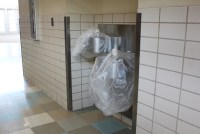 A photograph of a school hallway where two drinking fountains are stationed. They are covered up with plastic and unusable due to high levels of lead in the water.