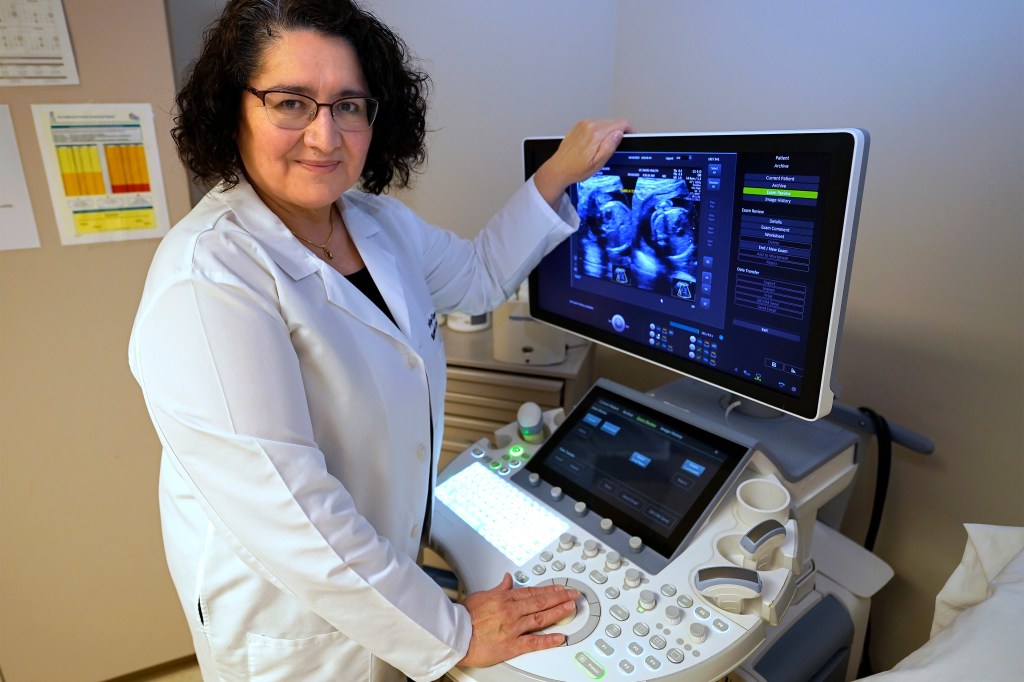 A photo of Carolina Reyes posing for a portrait by an ultrasound machine.