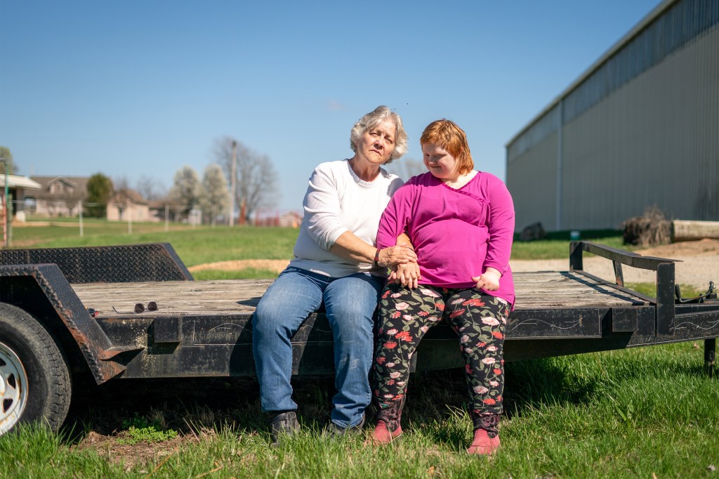 A photo of an older woman with her adult daughter sitting for a portrait outside by a barn.
