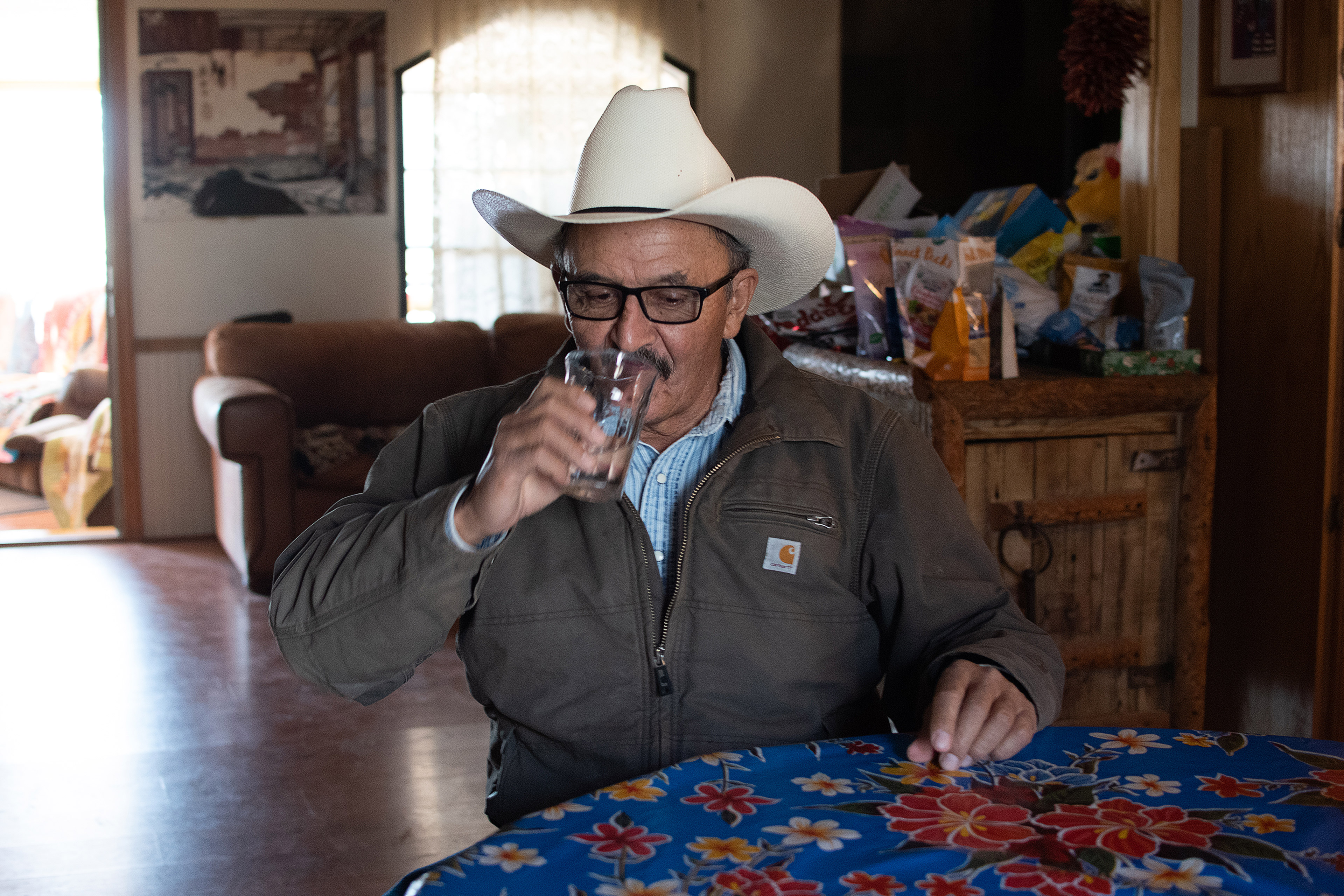A photo of John Mestas drinking a glass of water at a table indoors.