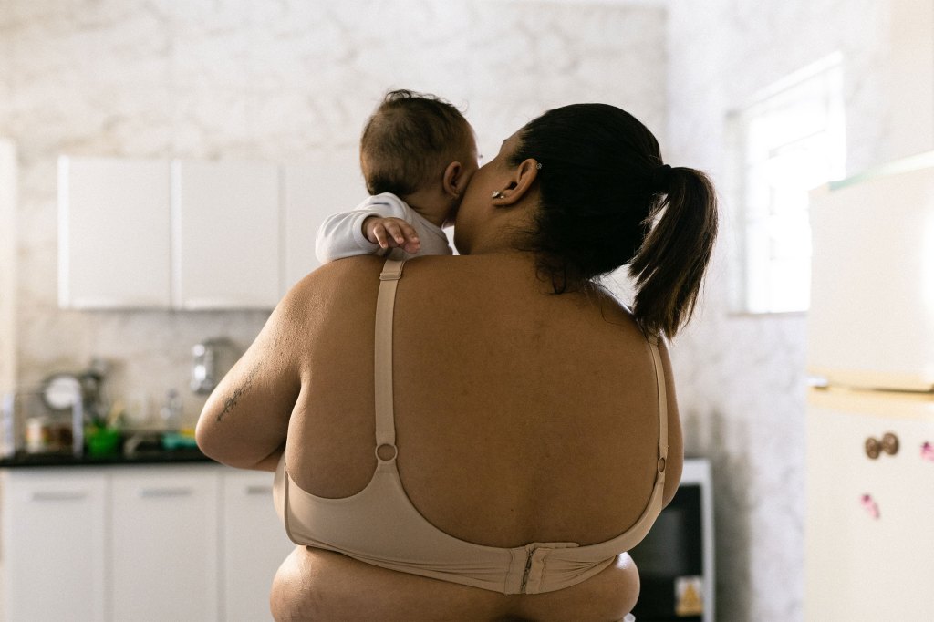 A view from behind of a woman wearing a bra and holding a baby to her cheek.