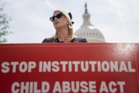 A photo of Paris Hilton standing behind a sign that reads, "Stop Institutional Child Abuse Act." The U.S. Capitol dome is seen behind her.