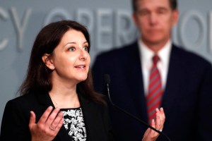 A photo of a woman talking at a press conference at a microphone.