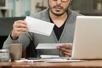 A photo of a man reviewing mail at a desk with a laptop.