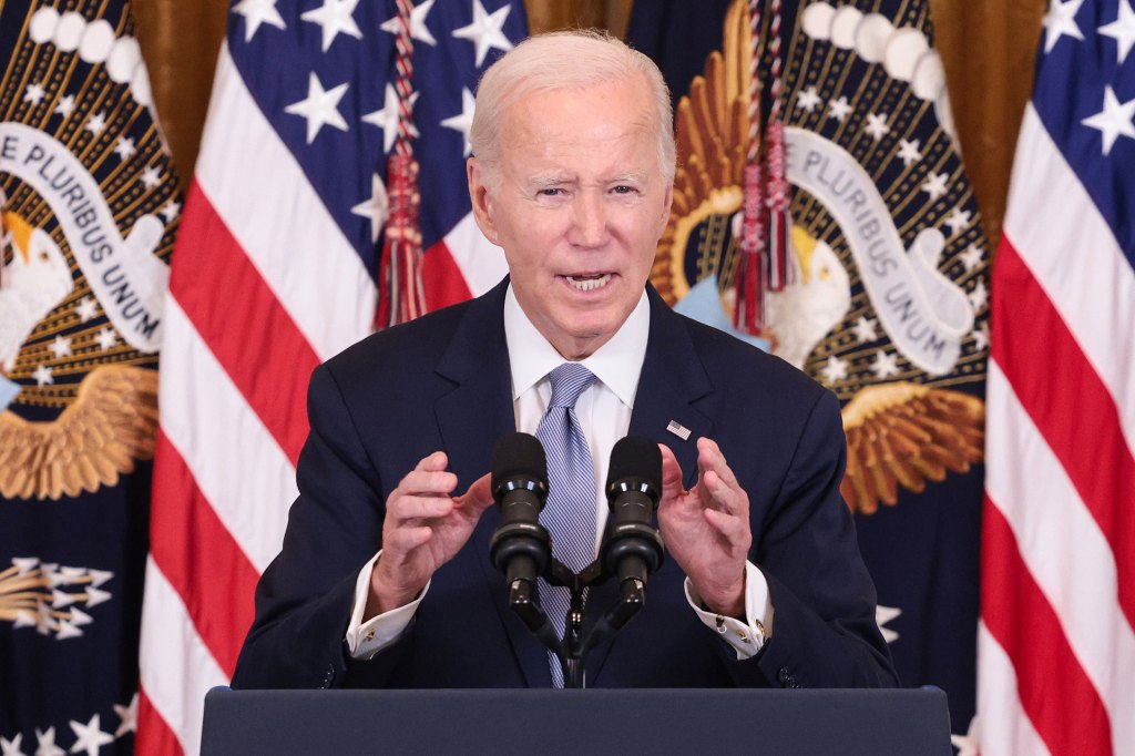 A photo of President Biden speaking at a podium in front of American flags.