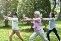 A photo of three older Asian women outside practicing tai chi.