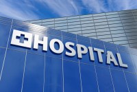 On the side of a hospital building, a large sign reads "HOSPITAL" under blue sky.