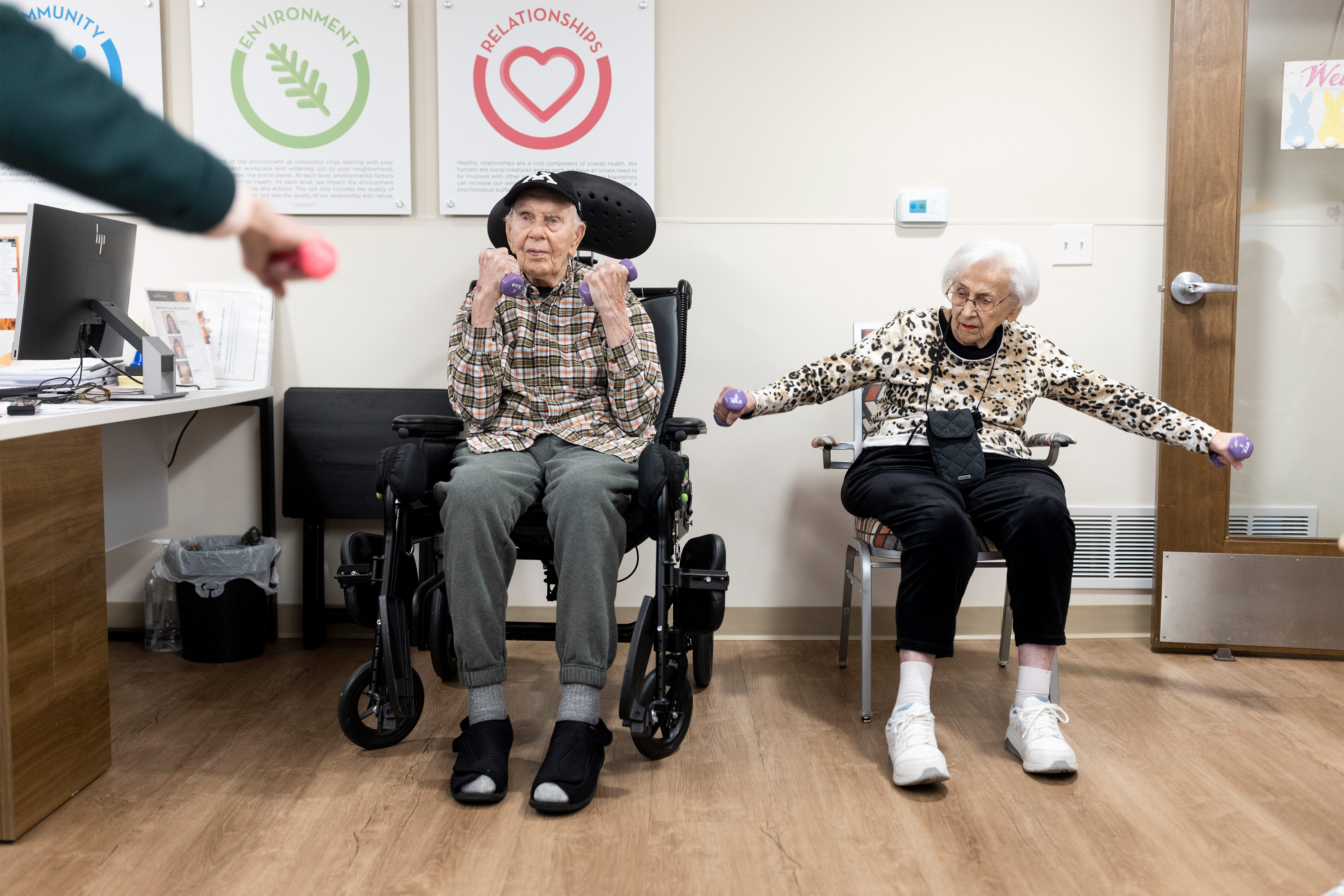 A photo of an elderly couple using small dumbbells to exercise while seated.