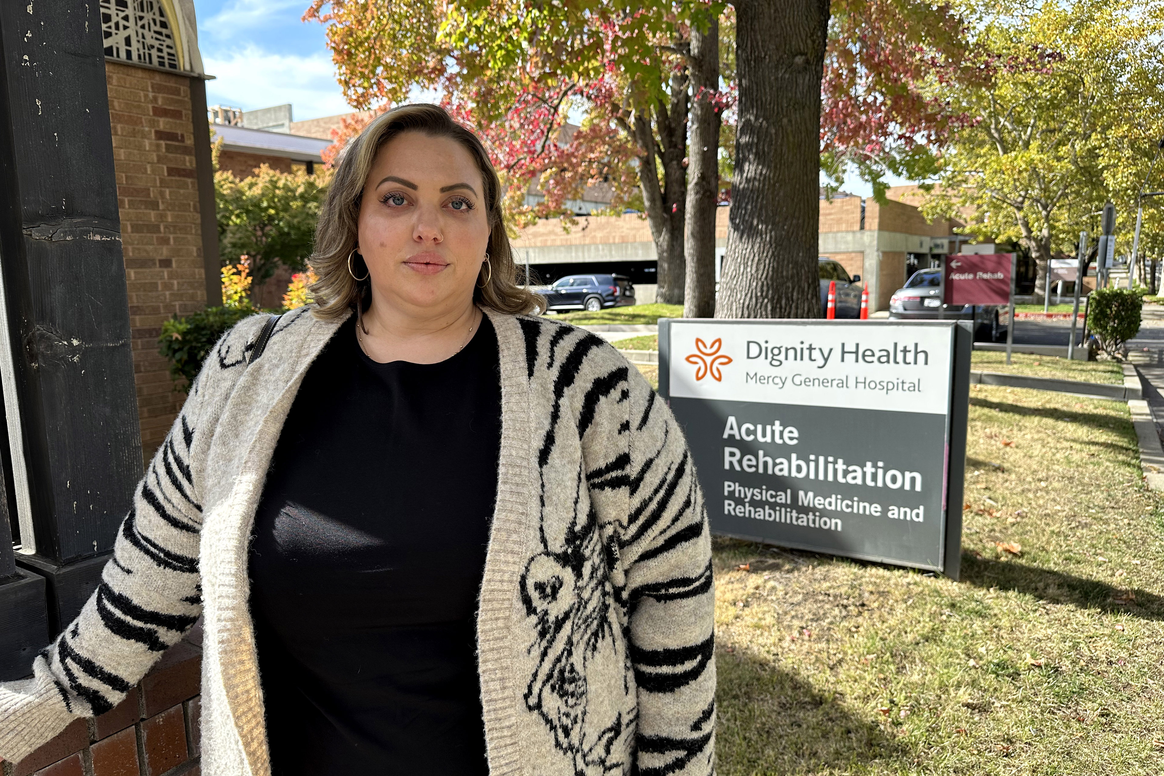 Terra Khan stands outside Mercy General Hospital on a sunny day. Behind her, a sign is visible. It reads, "Dignity Health / Mercy General Hospital / Acute Rehabilitation / Physical Medicine and Rehabilitation."