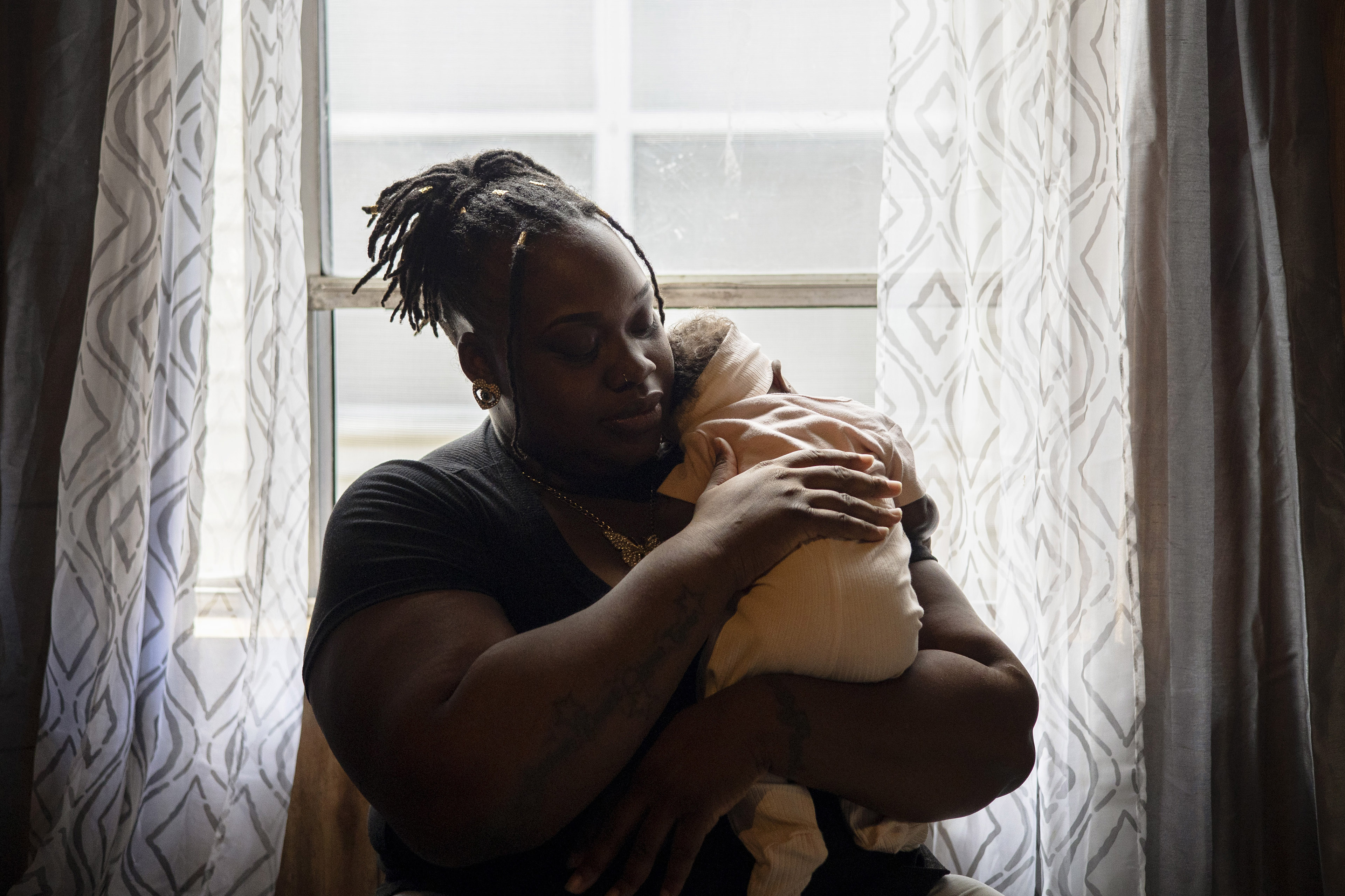 O’laysha Davis, standing in front of a window, holds her infant daughter in a gentle embrace.